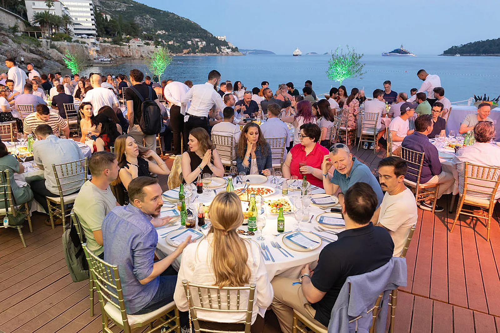 Long dinner tables on Banje beach at sunset, Dubrovnik's old town lit behind